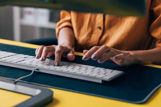 A woman diligently typing on a keyboard at her desk, showcasing concentration and productivity in her environment.